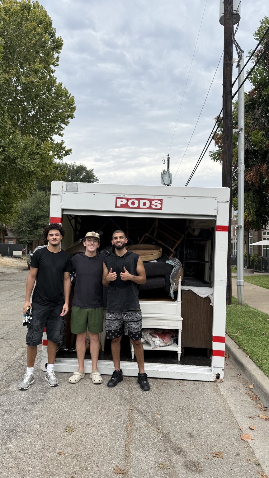 Three Nahas Moving movers standing in front of a packed PODS storage container on a residential street