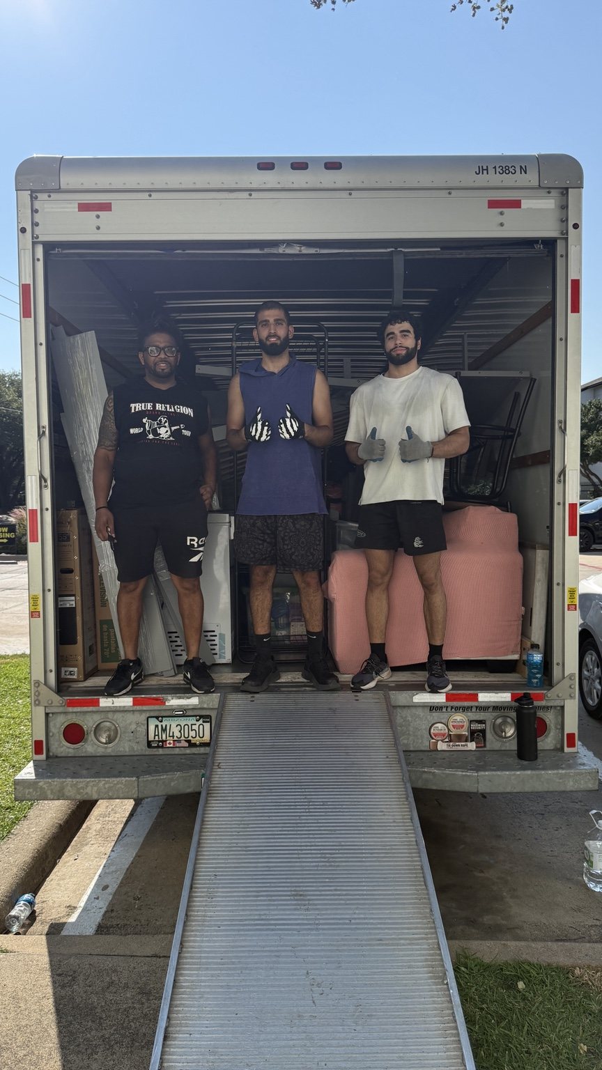 Three people standing inside the back of a loaded rental moving truck above the loading ramp