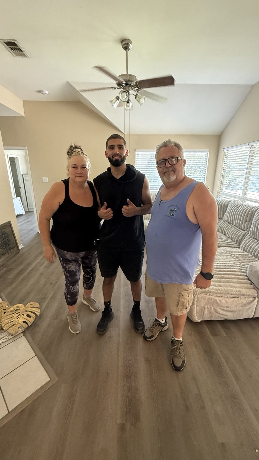 A Nahas Moving mover standing with two smiling customers in their living room after furniture was placed