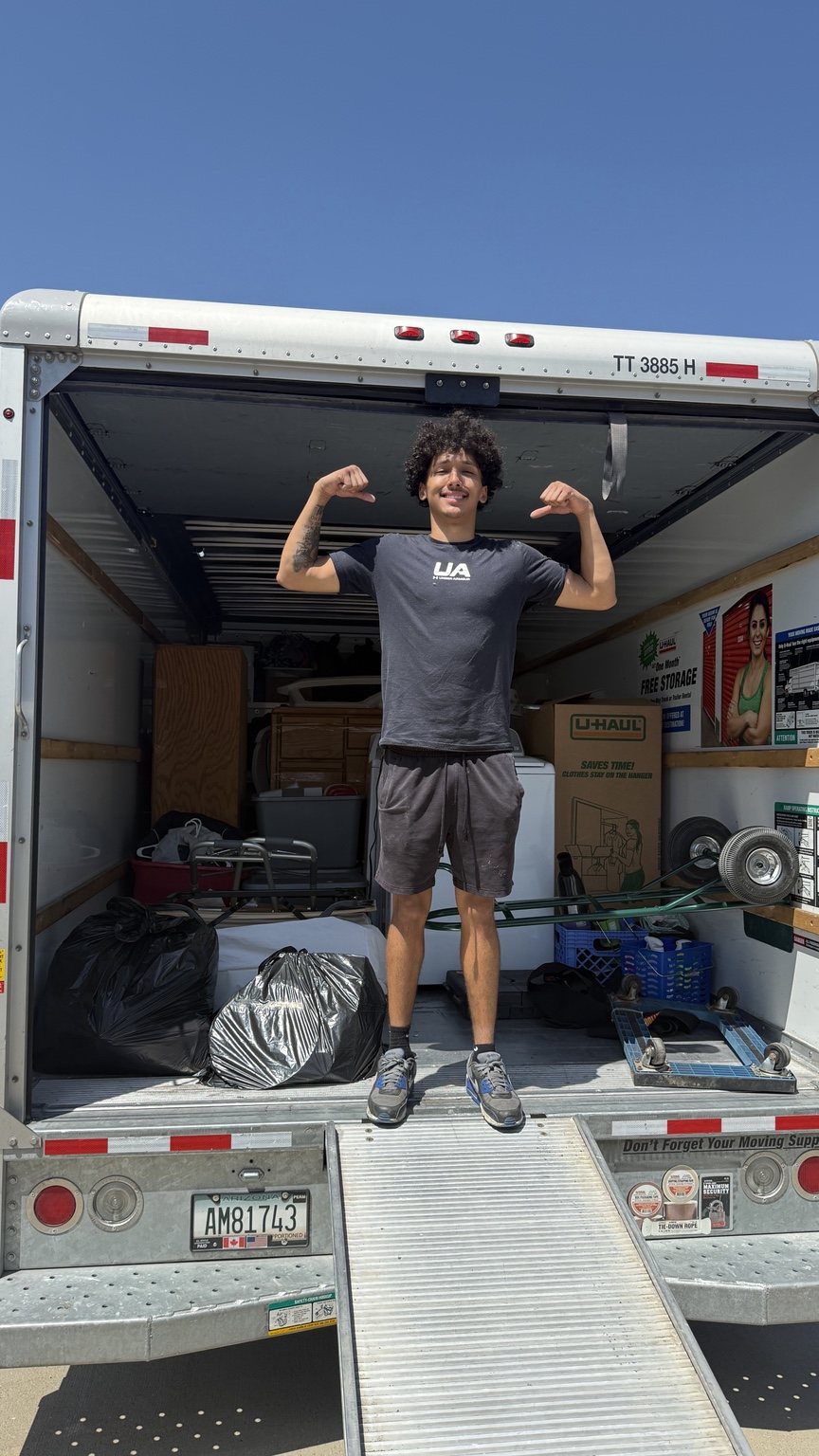 A Nahas Moving mover flexing inside a U-Haul truck loaded with furniture, boxes and a washer