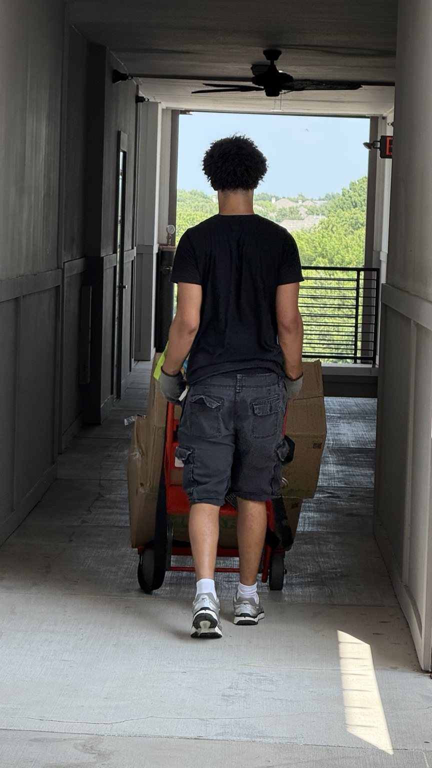 A Nahas Moving mover pulling a hand truck stacked with boxes down an apartment building breezeway